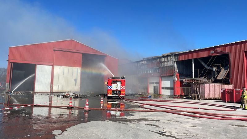 Brandweermensen blussen de loods waar nu minder rook te zien is 