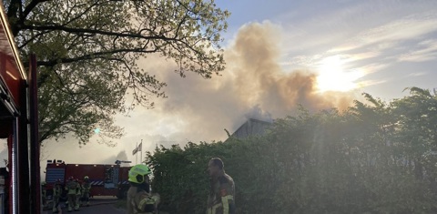 brandweervoertuigen staan opgesteld bij brandende loods