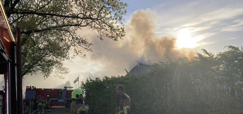 brandweervoertuigen staan opgesteld bij brandende loods